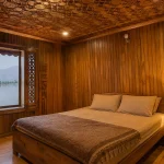 The carved wooden interior of a traditional Kashmir houseboat bedroom on Dal Lake, showing what a houseboat stay looks like
