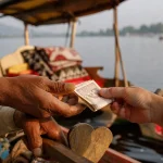 A tourist handing rupee notes to a Kashmiri shikara boatman on Dal Lake, an example of normal tipping in Kashmir